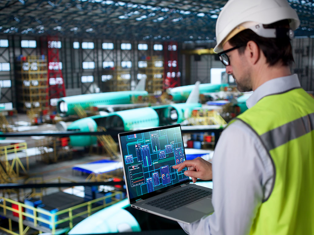 Messtechniker überprüft Maschinen in einem Luft- und Raumfahrtwerk mithilfe eines Laptops